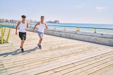 İki İspanyol erkek, sportif, gülümseyen bir çift, deniz kenarında koşuyorlar.