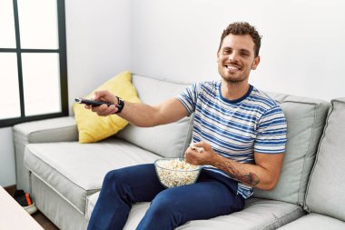 Genç İspanyol adam evde film izlerken kendine güvenerek gülümsüyor.