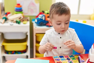 Adorable hispanic toddler playing with maths puzzle game sitting on table at kindergarten