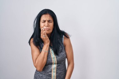 Beyaz arka planda dikilen olgun İspanyol kadın diş ağrısı ya da diş ağrısı yüzünden elleriyle dudaklarına dokunuyor. dişçi 
