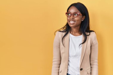 African young woman wearing glasses smiling looking to the side and staring away thinking. 