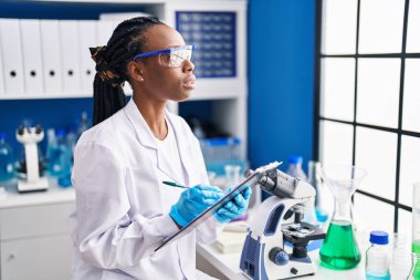 African american woman scientist writing on document at laboratory