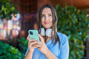 Genç, güzel, İspanyol bir kadın sokakta akıllı telefon kullanarak gülümsüyor.