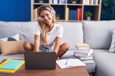 Kanepede oturan genç sarışın kız öğrenci evde ders çalışıyor.