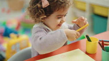 Adorable hispanic girl preschool student sitting on table drawing on paper at kindergarten