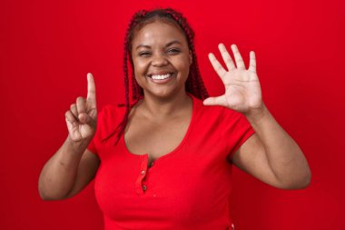 African american woman with braided hair standing over red background showing and pointing up with fingers number six while smiling confident and happy. 