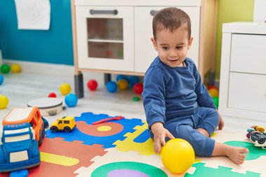 Tapılası İspanyol çocuk anaokulunda yerde kendinden emin bir şekilde otururken gülümsüyor.