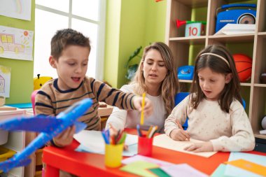 Teacher with boy and girl sitting on table drawing on paper at kindergarten
