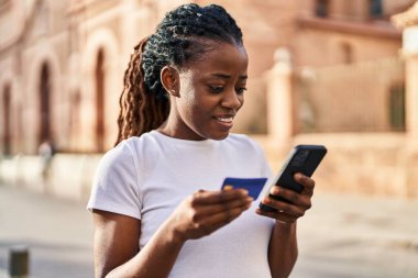 African american woman using smartphone and credit card at street