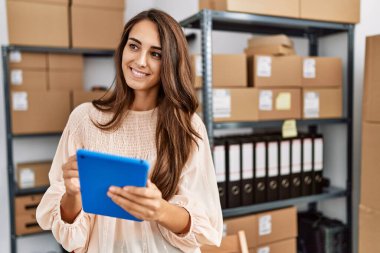 Young hispanic woman smiling confident using touchpad at storehouse