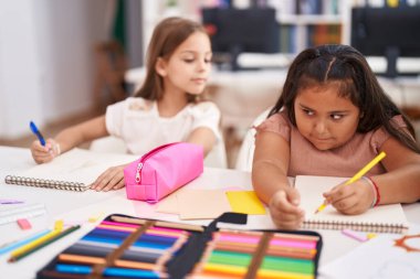 Two kids students sitting on table drawing on notebook paper at classroom