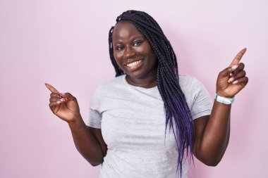 Pembe arka planda duran genç Afrikalı kadın farklı yönleri gösteren kendine güvenle gülümsüyor. reklam için kopyalama alanı 
