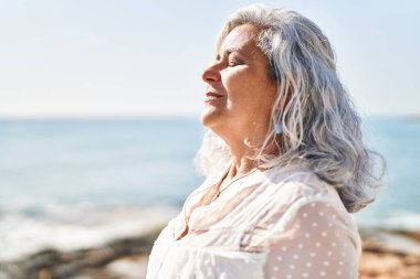 Middle age woman smiling confident breathing at seaside