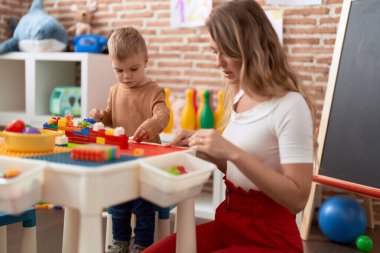 Teacher and toddler playing with construction blocks sitting on table at kindergarten