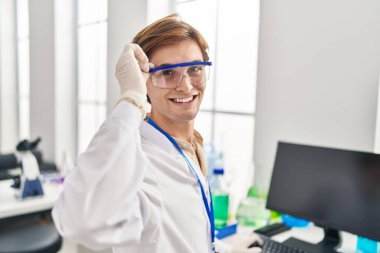 Young caucasian man scientist smiling confident using computer at laboratory