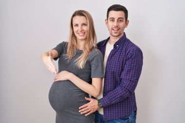 Genç bir çift beyaz arka planda duran bir bebek bekliyor. Dostça bir şekilde el sıkışarak selamlama ve hoş geldin diyorlar. başarılı iş. 