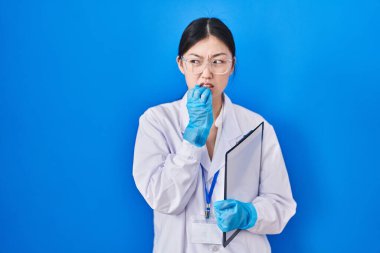 Chinese young woman working at scientist laboratory looking stressed and nervous with hands on mouth biting nails. anxiety problem. 