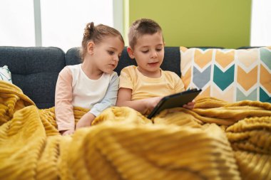 İki çocuk evdeki kanepede oturuyor.