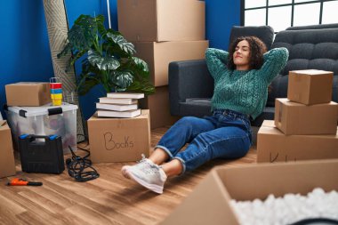 Genç, güzel, İspanyol bir kadın yeni evinde elleri başının üstünde yerde rahatça oturuyor.