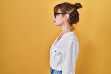 Sarı arka plan üzerine gündelik tişört giyen genç ve güzel bir kadın. Yan tarafa bakıyor, rahat bir görünüm takınıyor ve kendine güvenen bir gülümseme takınıyor.. 