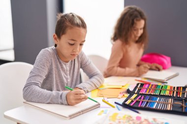 Two kids students sitting on table drawing on notebook paper at classroom