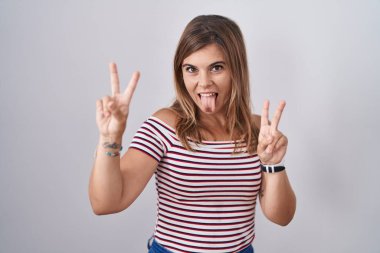 Soyutlanmış arka planda dikilen genç İspanyol kadın her iki elinde parmaklarını göstererek gülümseyerek zafer işareti yapıyor. İki numara.. 