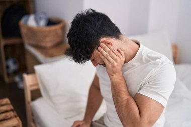 Young hispanic man suffering for backache sitting on bed at bedroom