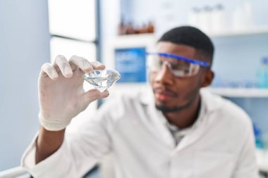 Laboratuvarda elmas tutan, bilim adamı üniforması giyen genç Afrikalı Amerikalı.