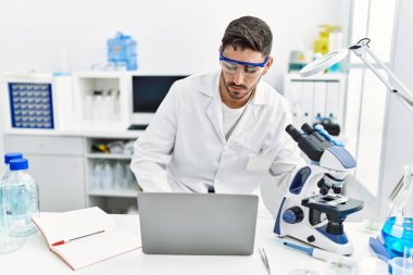 Mikroskop ve laptopla laboratuvarda bilimsel olarak çalışan yakışıklı bir İspanyol.