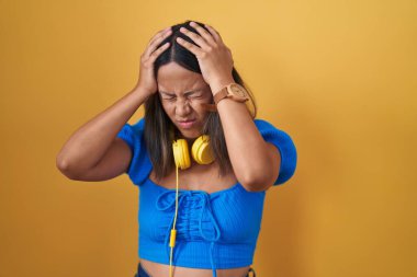 Hispanic young woman standing over yellow background suffering from headache desperate and stressed because pain and migraine. hands on head. 