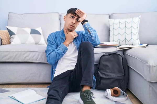 Young Hispanic Man Sitting Floor Studying University Touching Forehead Illness — Zdjęcie stockowe