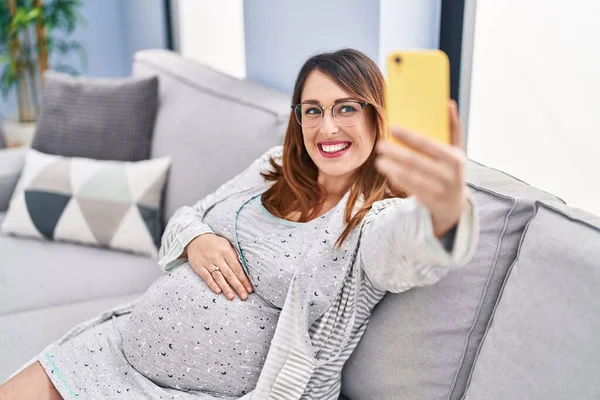 年轻的孕妇靠坐在家里沙发上的智能手机来自食其力 — 图库照片