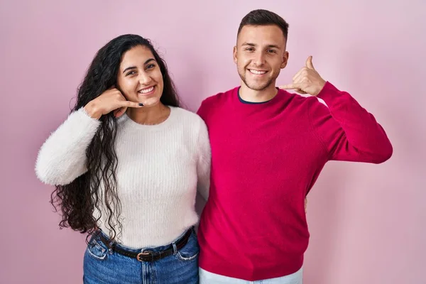 Young Hispanic Couple Standing Pink Background Smiling Doing Phone Gesture — Stockfoto