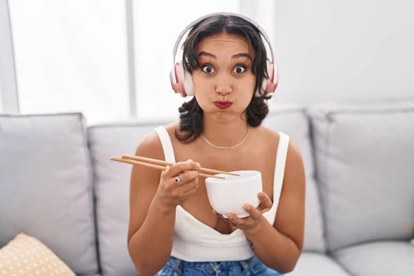 若いヒスパニック系の女性は面白い顔でお箸の頬をむいてアジア料理を食べています 空気を吸い込み空気を吸い込み — ストック写真