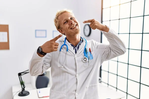 Młody Blondyn Noszący Mundur Lekarza Stetoskop Klinice Uśmiechający Się Radośnie — Zdjęcie stockowe