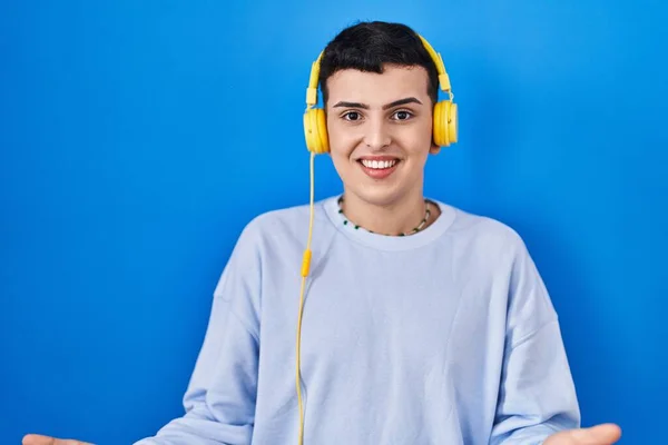 Non binary person listening to music using headphones smiling cheerful with open arms as friendly welcome, positive and confident greetings