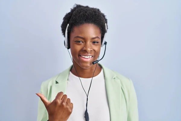 African american woman wearing call center agent headset pointing to the back behind with hand and thumbs up, smiling confident