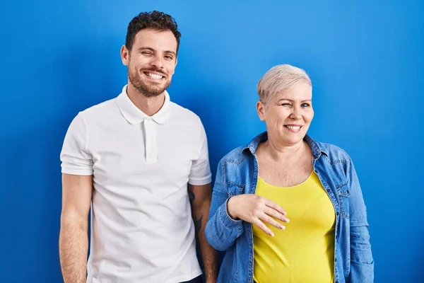 若いですブラジルの母親と息子立っています上の青の背景ウィンク見ますザカメラとともにセクシー表現 陽気で幸せな顔 — ストック写真
