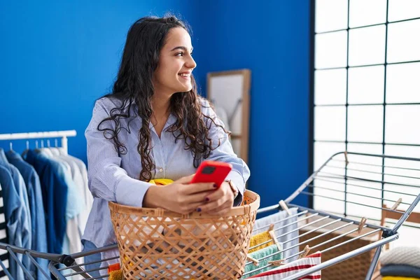 Young Hispanic Woman Using Smartphone Standing Laundry Room — Stockfoto