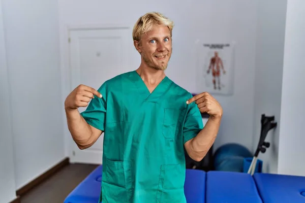 Young Blond Man Wearing Physiotherapist Uniform Standing Clinic Looking Confident — Stockfoto