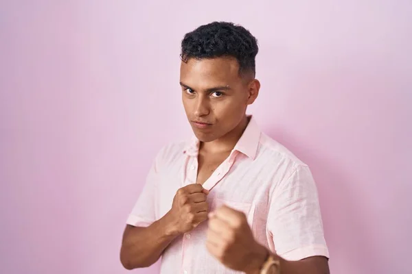 ピンクの背景に立っている若いヒスパニック系の男は 最初の防衛ジェスチャー 怒りと動揺の顔 問題を恐れて戦う準備ができて — ストック写真