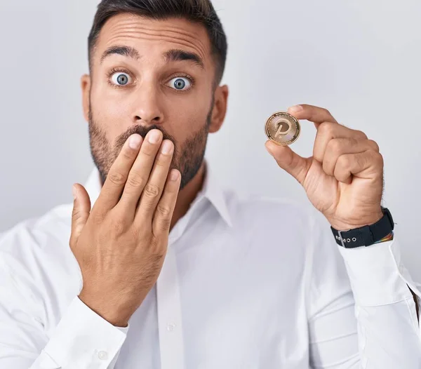 Handsome Hispanic Man Holding Polkadot Cryptocurrency Coin Covering Mouth Hand — Stock Photo, Image