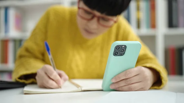 Young Chinese Woman Student Using Smartphone Writing Notebook Library University — ストック写真