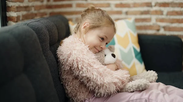 Adorable Blonde Girl Hugging Teddy Bear Sitting Sofa Home — Zdjęcie stockowe