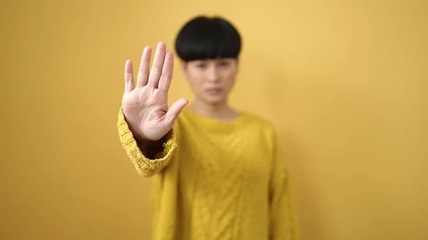 Young chinese woman doing stop gesture with hand over isolated yellow background