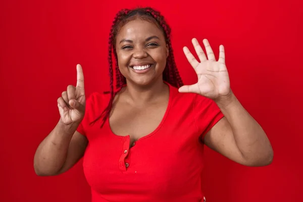 African american woman with braided hair standing over red background showing and pointing up with fingers number six while smiling confident and happy.