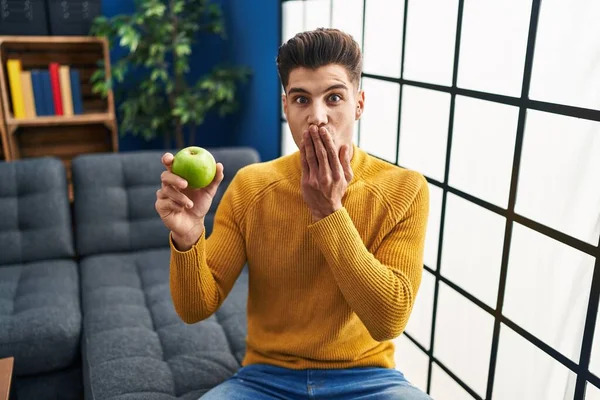 Młody Hiszpan Trzymający Zielone Jabłko Zakrywające Usta Dłonią Zszokowany Bojący — Zdjęcie stockowe