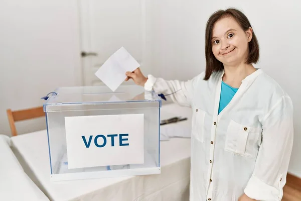 Brunette woman with down syndrome smiling putting envelope in ballot box at election room