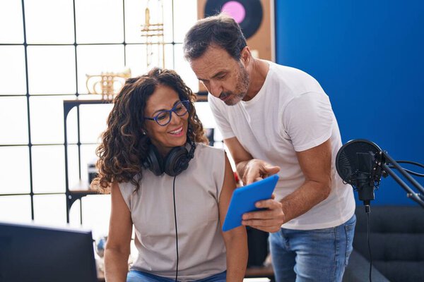 Man and woman musicians composing song using computer and touchpad at music studio