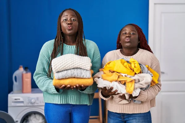 Two african women holding folded laundry after ironing looking at the camera blowing a kiss being lovely and sexy. love expression.